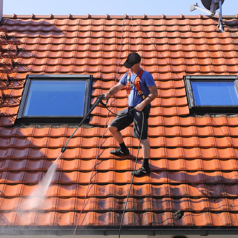 A worker using soft washing equipment to clean a house roof.